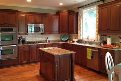 Inspiration for a mid-sized timeless u-shaped medium tone wood floor open concept kitchen remodel in Charlotte with an undermount sink, raised-panel cabinets, medium tone wood cabinets, granite countertops, white backsplash, subway tile backsplash, stainless steel appliances and an island