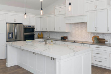 Photo of a large transitional kitchen in Orlando with a farmhouse sink, shaker cabinets, white cabinets, quartz benchtops, white splashback, marble splashback, stainless steel appliances, vinyl floors, with island, brown floor, white benchtop and vaulted.