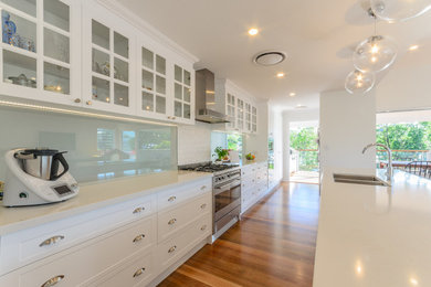 Photo of a large traditional galley open plan kitchen in Brisbane with an undermount sink, recessed-panel cabinets, white cabinets, marble benchtops, glass sheet splashback, stainless steel appliances, medium hardwood floors and with island.