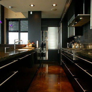 Idées déco pour une petite arrière-cuisine parallèle moderne avec un évier encastré, un placard à porte plane, des portes de placard noires, un plan de travail en granite, une crédence grise, une crédence en ardoise, un électroménager en acier inoxydable, béton au sol, un îlot central et un sol marron.