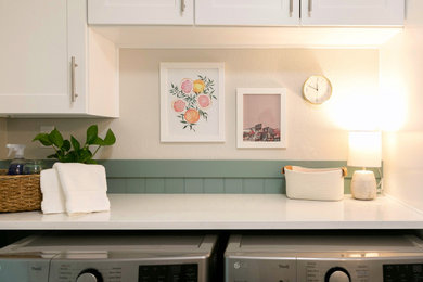 シアトルにあるトランジショナルスタイルのおしゃれなランドリールーム (I型、アンダーカウンターシンク、シェーカースタイル扉のキャビネット、白いキャビネット、クオーツストーンカウンター、緑のキッチンパネル、塗装板のキッチンパネル、緑の壁、クッションフロア、左右配置の洗濯機・乾燥機、グレーの床、白いキッチンカウンター、羽目板の壁) の写真