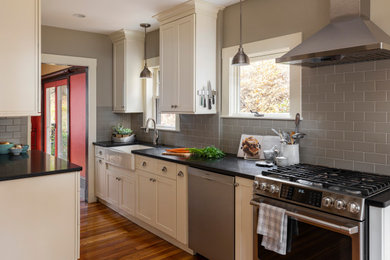 Kitchen - mid-sized transitional galley light wood floor kitchen idea in Boston with a farmhouse sink, shaker cabinets, white cabinets, granite countertops, gray backsplash, subway tile backsplash, stainless steel appliances, no island and black countertops