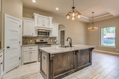 This is an example of a mid-sized traditional l-shaped open plan kitchen in Oklahoma City with an undermount sink, recessed-panel cabinets, granite benchtops, stainless steel appliances, with island, white cabinets, beige splashback, porcelain splashback, light hardwood floors and beige floor.