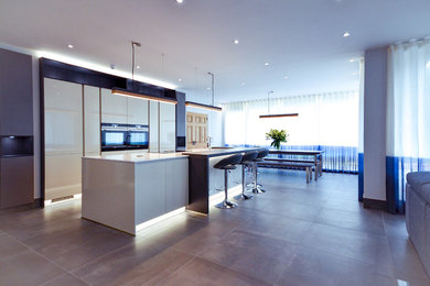 Photo of a large contemporary galley eat-in kitchen in Glasgow with a single-bowl sink, flat-panel cabinets, white cabinets, glass benchtops, white splashback, glass tile splashback, black appliances, marble floors, with island and multi-coloured floor.