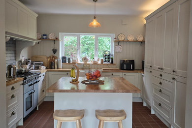 Inspiration for a medium sized country u-shaped kitchen/diner in West Midlands with a belfast sink, shaker cabinets, beige cabinets, wood worktops, grey splashback, ceramic splashback, stainless steel appliances, terracotta flooring, an island, brown floors, brown worktops and a coffered ceiling.