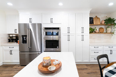 ロサンゼルスにある高級な広いトランジショナルスタイルのおしゃれなキッチン (エプロンフロントシンク、レイズドパネル扉のキャビネット、白いキャビネット、クオーツストーンカウンター、ベージュキッチンパネル、セラミックタイルのキッチンパネル、シルバーの調理設備、クッションフロア、茶色い床、白いキッチンカウンター) の写真