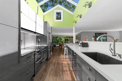 Design ideas for a contemporary galley open plan kitchen in Sydney with an undermount sink, flat-panel cabinets, grey cabinets, stainless steel appliances, dark hardwood floors, with island, brown floor and white benchtop.