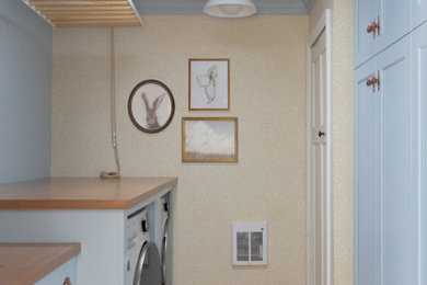 Utility room - mid-sized traditional galley terra-cotta tile, brown floor and wallpaper utility room idea in Detroit with shaker cabinets, blue cabinets, wood countertops, yellow walls, a side-by-side washer/dryer and brown countertops