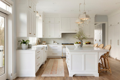 Huge elegant u-shaped light wood floor and brown floor eat-in kitchen photo in Minneapolis with a farmhouse sink, recessed-panel cabinets, white cabinets, quartz countertops, white backsplash, quartz backsplash, white appliances, an island and white countertops