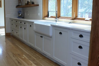 Example of a mid-sized arts and crafts l-shaped light wood floor and beige floor eat-in kitchen design in Calgary with a farmhouse sink, shaker cabinets, white cabinets, quartz countertops, white backsplash, ceramic backsplash, stainless steel appliances, an island and gray countertops