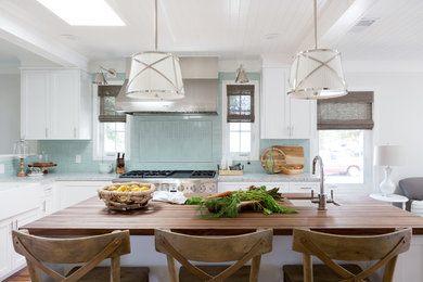 This is an example of a beach style l-shaped open plan kitchen in Los Angeles with a farmhouse sink, shaker cabinets, white cabinets, granite benchtops, blue splashback, glass tile splashback, stainless steel appliances, with island and medium hardwood floors.
