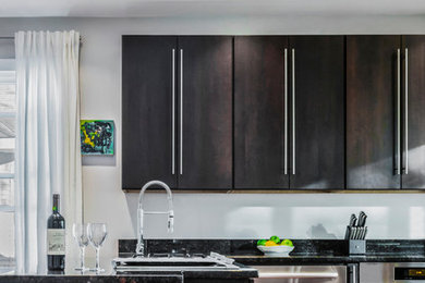 Example of a trendy u-shaped medium tone wood floor kitchen design in Providence with a double-bowl sink, flat-panel cabinets, dark wood cabinets, granite countertops, brown backsplash, stainless steel appliances and a peninsula
