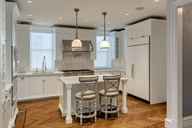 Large elegant medium tone wood floor kitchen photo in New York with an undermount sink, raised-panel cabinets, white cabinets, marble countertops, stone tile backsplash, paneled appliances and an island