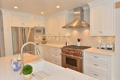 Kitchen - transitional l-shaped brown floor and medium tone wood floor kitchen idea in New York with a farmhouse sink, flat-panel cabinets, white cabinets, quartz countertops, gray backsplash, ceramic backsplash, stainless steel appliances, an island and multicolored countertops