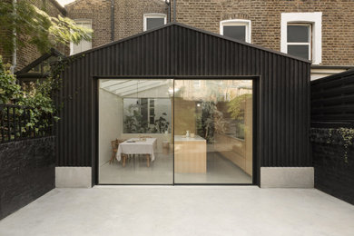 Photo of a medium sized and black scandi rear house exterior in London with three floors, wood cladding, a pitched roof, a grey roof and board and batten cladding.