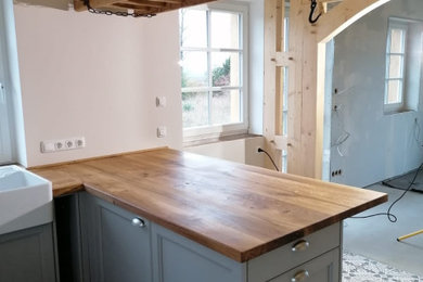 Offene, Mittelgroße Country Küche in U-Form mit Doppelwaschbecken, Kassettenfronten, grauen Schränken, Arbeitsplatte aus Holz, Porzellan-Bodenfliesen, Halbinsel, grauem Boden und freigelegten Dachbalken in Berlin