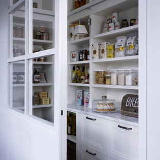 Minimalistisk inredning av ett litet kök, med en undermonterad diskho, vita skåp, marmorbänkskiva, vitt stänkskydd, stänkskydd i sten, vita vitvaror, ljust trägolv, en köksö och luckor med infälld panel