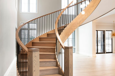 Diseño de escalera curva minimalista grande con escalones de madera, contrahuellas de madera y barandilla de madera