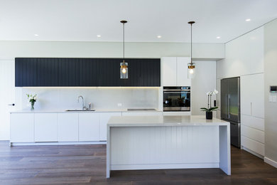 Inspiration for an expansive modern galley open plan kitchen in Sydney with an undermount sink, flat-panel cabinets, white cabinets, quartz benchtops, white splashback, stone slab splashback, stainless steel appliances, medium hardwood floors, with island, brown floor and white benchtop.