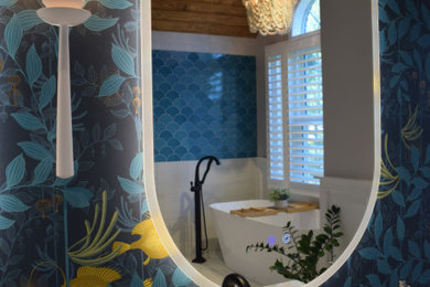 This is an example of a large coastal ensuite bathroom in Baltimore with freestanding cabinets, light wood cabinets, a freestanding bath, a walk-in shower, a two-piece toilet, blue tiles, porcelain tiles, grey walls, porcelain flooring, a submerged sink, marble worktops, white floors, an open shower, white worktops, a wall niche, double sinks, a freestanding vanity unit, a timber clad ceiling and wallpapered walls.