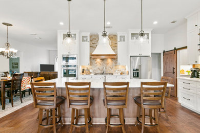 Example of a farmhouse l-shaped medium tone wood floor and brown floor kitchen design in Dallas with an undermount sink, shaker cabinets, white cabinets, beige backsplash, an island and white countertops