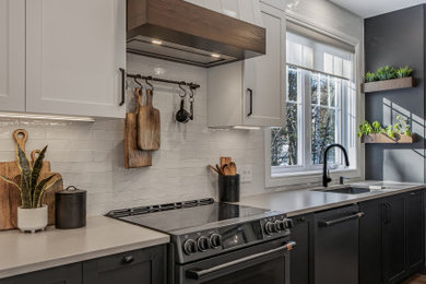 Example of a large trendy l-shaped dark wood floor and brown floor open concept kitchen design in Montreal with an integrated sink, shaker cabinets, black cabinets, quartzite countertops, black appliances, an island and beige countertops