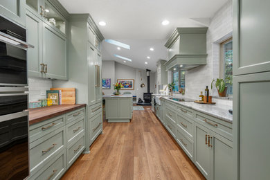 Open concept kitchen - huge transitional galley medium tone wood floor and brown floor open concept kitchen idea in Portland with a farmhouse sink, beaded inset cabinets, green cabinets, quartzite countertops, white backsplash, ceramic backsplash, paneled appliances, an island and gray countertops