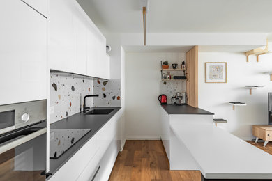 Cette photo montre une cuisine ouverte parallèle moderne de taille moyenne avec un évier encastré, une crédence multicolore, un électroménager noir, parquet foncé, îlot et plan de travail noir.
