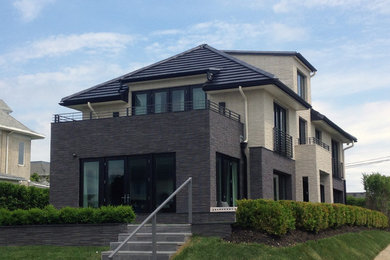 Example of a large trendy beige three-story stone house exterior design in New York with a hip roof and a tile roof