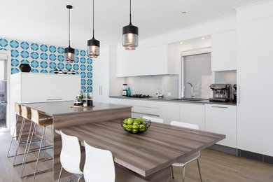 Photo of a large contemporary galley eat-in kitchen in Other with an undermount sink, white cabinets, quartz benchtops, white splashback, glass sheet splashback, stainless steel appliances, light hardwood floors and with island.