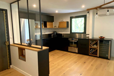 Cette image montre une grande cuisine ouverte minimaliste en L avec des portes de placard noires, un plan de travail en granite, une crédence métallisée et plan de travail noir.