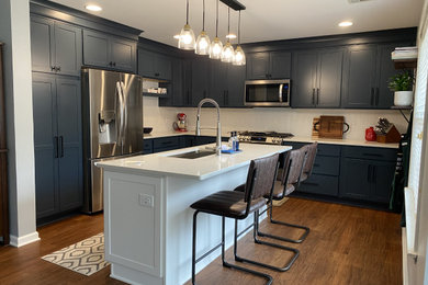 Example of a mid-sized transitional u-shaped brown floor enclosed kitchen design in Other with an undermount sink, shaker cabinets, blue cabinets, quartz countertops, white backsplash, stainless steel appliances, an island and white countertops