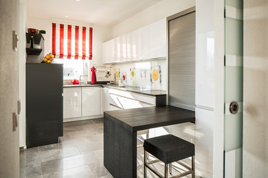 Geschlossene, Kleine Moderne Küche in U-Form mit Einbauwaschbecken, flächenbündigen Schrankfronten, weißen Schränken, Marmor-Arbeitsplatte, Küchenrückwand in Weiß, Glasrückwand, Schieferboden, Halbinsel, grauem Boden und schwarzer Arbeitsplatte in München