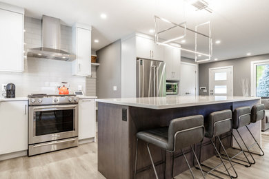 Inspiration for a mid-sized contemporary l-shaped medium tone wood floor and brown floor open concept kitchen remodel in Calgary with an island, an undermount sink, white cabinets, quartz countertops, white backsplash, porcelain backsplash, stainless steel appliances and white countertops