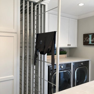 ミルウォーキーの中サイズのトランジショナルスタイルのおしゃれな家事室 (エプロンフロントシンク、落し込みパネル扉のキャビネット、白いキャビネット、グレーの壁、セラミックタイルの床、目隠し付き洗濯機・乾燥機、茶色い床、グレーのキッチンカウンター) の写真