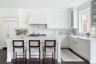 Design ideas for a transitional l-shaped kitchen in Seattle with a farmhouse sink, shaker cabinets, white cabinets, white splashback, stone slab splashback, panelled appliances, dark hardwood floors, with island and white benchtop.