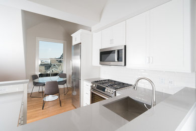 Small transitional u-shaped kitchen in San Francisco with an undermount sink, shaker cabinets, white cabinets, quartz benchtops, white splashback, subway tile splashback, stainless steel appliances, light hardwood floors, with island and brown floor.