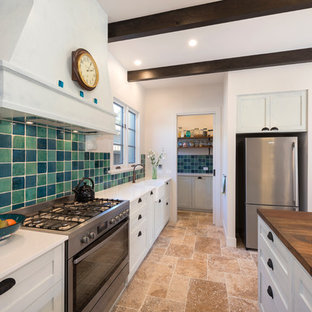 Идея дизайна: большая параллельная кухня в средиземноморском стиле с кладовкой, раковиной в стиле кантри, фасадами в стиле шейкер, белыми фасадами, разноцветным фартуком, техникой из нержавеющей стали, полом из травертина, островом, фартуком из терракотовой плитки и столешницей из кварцевого композита