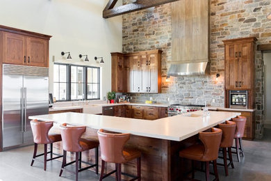 Example of a cottage l-shaped gray floor kitchen design in Other with a farmhouse sink, shaker cabinets, medium tone wood cabinets, gray backsplash, stone tile backsplash, stainless steel appliances, an island and beige countertops