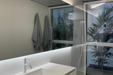 Modelo de cuarto de baño único moderno de tamaño medio con armarios con paneles lisos, puertas de armario blancas, ducha a ras de suelo, baldosas y/o azulejos blancos, aseo y ducha, ducha abierta y encimeras blancas