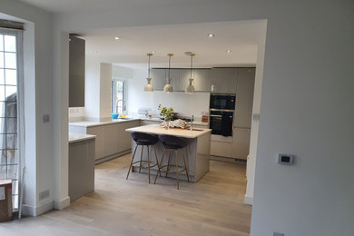 Inspiration for a large modern grey and white open plan kitchen in London with a double-bowl sink, flat-panel cabinets, grey cabinets, quartz worktops, integrated appliances, laminate floors, an island, grey floors, white worktops and feature lighting.
