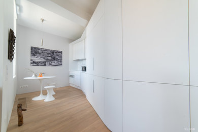 Inspiration for a mid-sized contemporary single-wall open plan kitchen in Strasbourg with light hardwood floors, an integrated sink, beaded inset cabinets, white cabinets, no island and white benchtop.