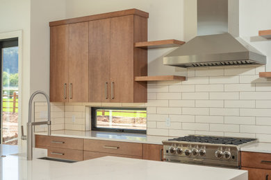 Design ideas for an expansive contemporary l-shaped open plan kitchen in Denver with a belfast sink, flat-panel cabinets, medium wood cabinets, quartz worktops, white splashback, metro tiled splashback, stainless steel appliances, light hardwood flooring, an island, white worktops and exposed beams.
