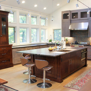 Inspiration pour une grande cuisine ouverte traditionnelle en U avec un évier 3 bacs, un plan de travail en granite, un électroménager en acier inoxydable, un sol en bois clair, un îlot central, un placard avec porte à panneau encastré, des portes de placard en bois vieilli et une crédence en carrelage de pierre.