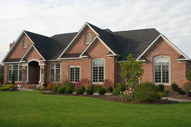 Large elegant red two-story brick exterior home photo in New York with a clipped gable roof