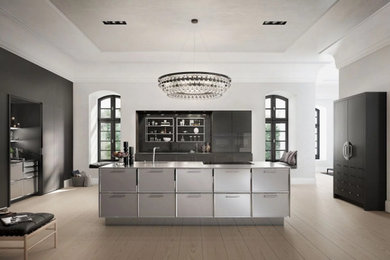 This is an example of a contemporary open plan kitchen in Essex with stainless steel cabinets, light hardwood flooring, an island and brown floors.