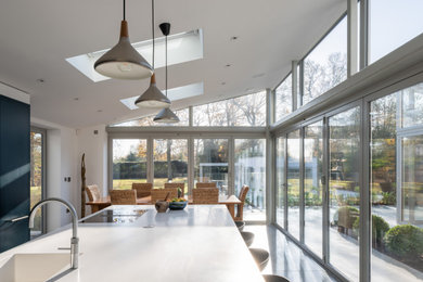 Moderne Wohnküche mit Mineralwerkstoff-Arbeitsplatte, Betonboden, Kücheninsel, weißer Arbeitsplatte und gewölbter Decke in Hertfordshire