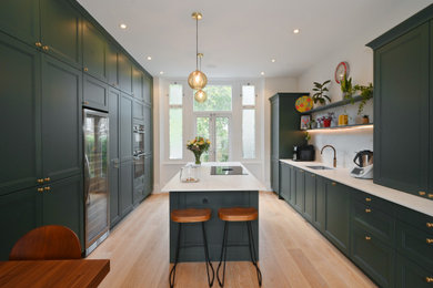This is an example of a large classic kitchen/diner in London with a single-bowl sink, shaker cabinets, green cabinets, quartz worktops, white splashback, an island and white worktops.