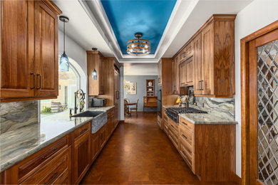 Large elegant galley cork floor, brown floor and tray ceiling eat-in kitchen photo in Santa Barbara with a farmhouse sink, raised-panel cabinets, medium tone wood cabinets, quartzite countertops, multicolored backsplash, paneled appliances, no island, multicolored countertops and stone slab backsplash