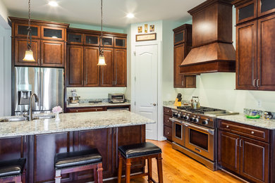 Large traditional l-shaped eat-in kitchen in Baltimore with medium wood cabinets, quartzite benchtops, white splashback, stainless steel appliances, with island, an undermount sink, raised-panel cabinets and medium hardwood floors.